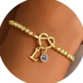 Elegante bracciale perle oro nodo cuore con ciondolo lettera L e variante pietra natale. - Lettera A / Giugno (Color Pietra di Luna)