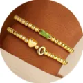 Bracciale di perline dorate con pietra verde, ciondolo a cuore e lettera elegante. - Lettera A / Agosto