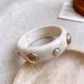 Primer plano detallado de pulsera de resina beige con concha dorada y perlas finas. - Seashell Decorated Bangle / Blanco Roto