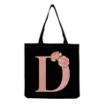 Close-up detail of black canvas tote bag featuring pink letter D print and floral decoration. - Letter D Style (hmk2865)