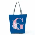 Blue tote bag detail showing pink letter G and white floral print, grey shoulder straps. - Letter G
