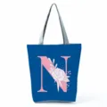 Detailed view of blue tote bag featuring pink letter N floral print and secure zipper. - Letter N