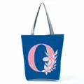 Blue canvas tote bag detail featuring a large pink letter O and elegant white floral print. - Letter O