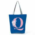 Blue canvas tote bag featuring a pink letter Q and floral print with grey shoulder straps detail. - Letter Q