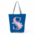 Blue canvas tote bag with pink letter S and floral print, zipper closure and grey straps. - Letter S