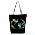 Detalle de estampado de colibrí en bolso tote negro de lona, patrón floral colorido y asas grises. - Bolso Tote de Hombro (hlk2791) / Estampado Colibrí Negro Guirnalda (hlk2791)