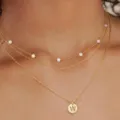 Collana multistrato dorata con perle delicate ed elegante ciondolo con moneta iniziale. - Oro W