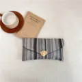 Stylish woven envelope clutch bag with unique gold metal clasp, elegant color block design. - Black