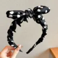 Black and white polka dot headband with comb teeth and bow, stylish hair accessory. - Black