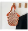 Vista detallada del elegante bolso de malla de cuero naranja y beige colgado en gancho. - Naranja