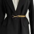 Close-up detail of stylish women's black elastic and gold metal chain belt worn over suit. - Gold