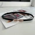 Close-up detail of a black thin belt featuring an elegant gold leaf buckle and adjustable fit. - Black