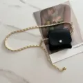 Detail shot of stylish black mini waist bag with gold woven chain belt, trendy accessory. - White