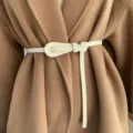 Close-up detail of women's thin decorative belt with oval buckle on winter coat, elegant style. - Beige