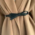 Close up detail of women's black faux leather bowknot belt styled on a camel wool coat. - Black
