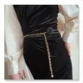 Close-up view of the elegant black camellia flower and gold chain belt detail accessory. - Black