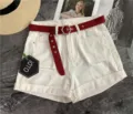 Close-up of white denim shorts featuring a red canvas belt and unique hexagonal metal buckle. - 105cm / Red