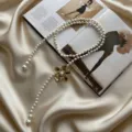 Close-up of elegant pearl waist chain with a gold flower pendant on luxury satin fabric. - Gold