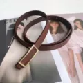 Brown leather belt close-up, featuring a minimalist rectangular gold-tone metal buckle detail. - Coffee