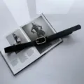 Detail view of a stylish black leather belt featuring a sleek golden square buckle. - Black