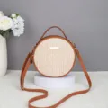 Detailed view of the chic round straw crossbody bag with brown leather trim and shoulder strap. - 17*6*17 / Tan