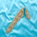 Detailed view of sparkling rhinestone bridal belt applique with gold backing on blue satin fabric. - Gold