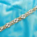 Detailed shot of sparkling rhinestone belt applique with clear crystals and pearls on blue satin. - Gold