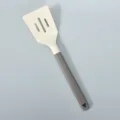 Silikonschlitzlöffel mit grauem Griff und cremeweissem Kopf zum Kochen und Braten. - Creme