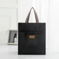 Black canvas student tote bag with striped handles and front pocket for lunch box or books. - Black Medium