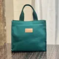 Vista dettagliata di una borsa porta pranzo in tela verde scuro con etichetta in pelle. - Targhetta verde