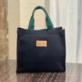 Gedetailleerd aanzicht van canvas lunchtas met groene handvatten en sterke stofkwaliteit. - Zwart label