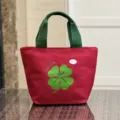 Compact canvas lunch bag in vibrant red with green handles, featuring a clover print for daily use. - Lucky Clover / Red