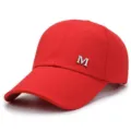Red canvas baseball cap detail showing silver metal M logo and curved brim design. - Red