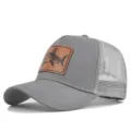 Detalle de gorra trucker gris de malla, con parche de cuero marrón y llamativo diseño de tiburón. - Ajustable / Gris claro