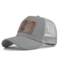 Detail view of gray trucker hat featuring a textured brown leather patch with raccoon graphic. - Adjustable / Light Gray