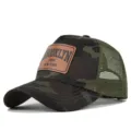 Close up detail of camouflage mesh trucker hat featuring brown leather Brooklyn patch. - Grey Camouflage
