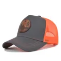 Detalle en primer plano de la gorra trucker gris y naranja con un parche de cuero distintivo. - Gris Oscuro y Malla Naranja