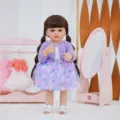 Detailed view of a 22-inch reborn baby doll with brown pigtails wearing a purple butterfly dress. - Purple Knit Cardigan Butterfly Dress Style (Q22-005-045) / 55cm