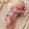 Detailed close-up of a 45cm sleeping reborn baby doll wearing floral romper and flower headband. - Pink Rose Print Style (Q18-073-067)