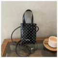 Primer plano detallado del pequeño bolso negro de mano con lunares blancos y textura. - Negro