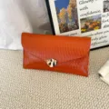 Orange textured envelope clutch bag featuring a sleek abstract gold metal clasp detail. - Orange