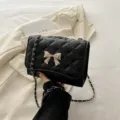 Black quilted chain shoulder bag for women, stylish crossbody bag with metal bow accent. - Black