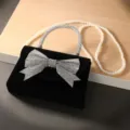 Mooi detail van de zwarte fluwelen avondtas met strass-strik en elegante parelketting. - Parelketing / Zwart