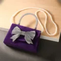 Paarse fluwelen avondtas detail met sprankelende strass strik en elegante parelketting. - Parelketing / Paars