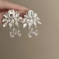 Close-up detail of silver-tone rhinestone cluster earrings with hanging crystal teardrops. - Silver Rhinestone Flower Sterling Silver Post Earrings