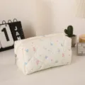 Primer plano del neceser acolchado con flores, mostrando textura suave y costuras finas. - Amarillo