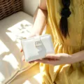 Close-up detail of the minimalist white bifold wallet featuring an elegant gold square buckle. - Off White