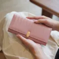 Detailansicht einer rosa Geldbörse mit Streifen und goldenem Verschluss in den Händen gehalten. - Rosa
