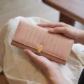 Vue détaillée du portefeuille long rose avec des rayures verticales et un fermoir doré. - Abricot