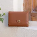 Detailed shot of brown tri-fold wallet with elegant metal buckle against rustic wall. - Brown
